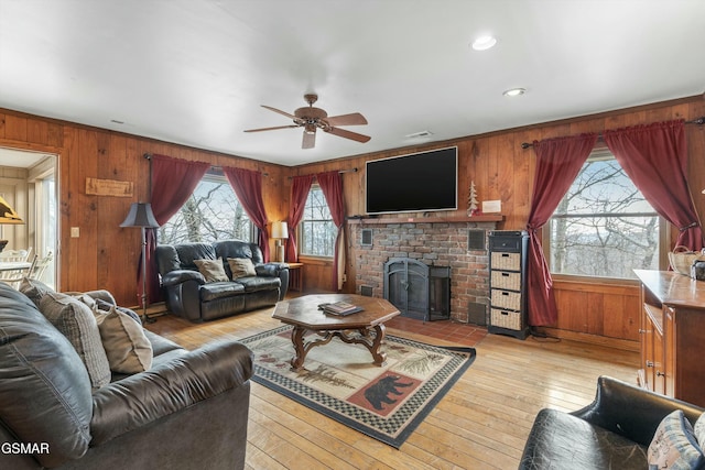 living area featuring light wood-style floors, a brick fireplace, ceiling fan, and wood walls