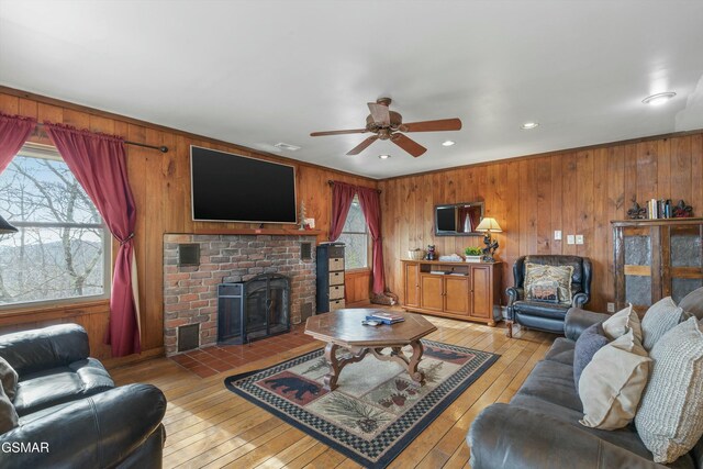 living area with a ceiling fan, light wood-type flooring, a fireplace, and wooden walls