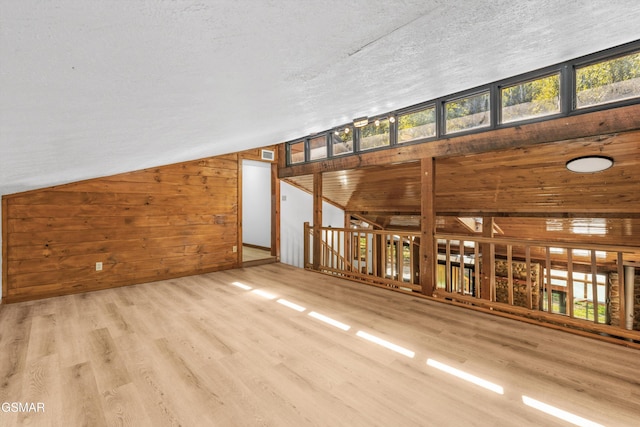 unfurnished living room featuring lofted ceiling, a textured ceiling, wooden walls, wood finished floors, and visible vents