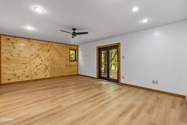 empty room featuring wood walls, light wood-style flooring, baseboards, and recessed lighting