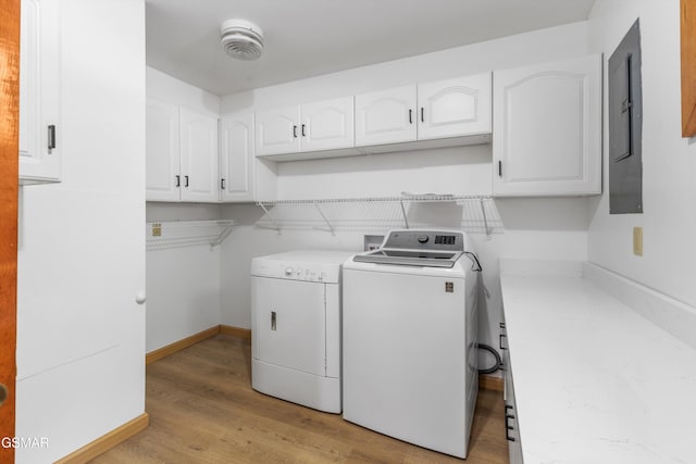 washroom with cabinet space, electric panel, baseboards, washer and clothes dryer, and light wood-type flooring