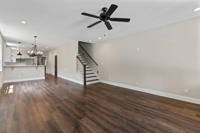 unfurnished living room with ceiling fan with notable chandelier and dark wood-type flooring