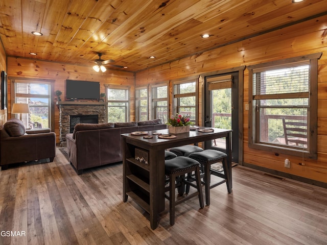 dining space with hardwood / wood-style floors, wooden ceiling, a fireplace, and wooden walls