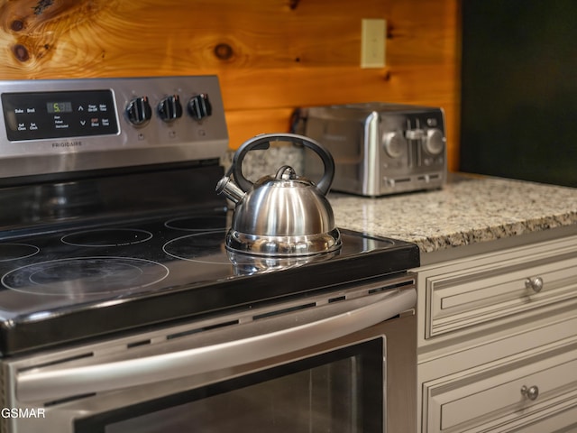 kitchen featuring stainless steel electric range, wood walls, and light stone counters