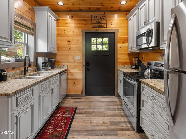 kitchen featuring wood walls, white cabinets, sink, light stone counters, and stainless steel appliances