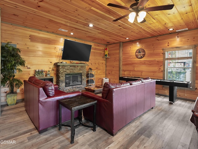 living room with hardwood / wood-style floors, wood walls, a stone fireplace, and wooden ceiling