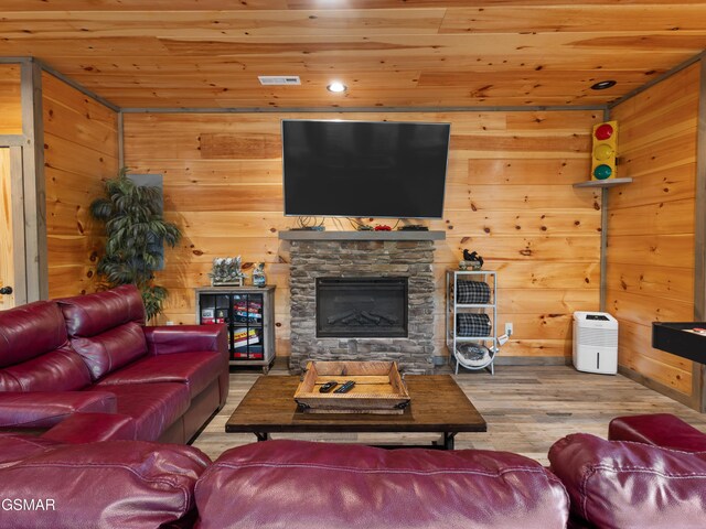 living room featuring hardwood / wood-style flooring, wood walls, a stone fireplace, and wooden ceiling