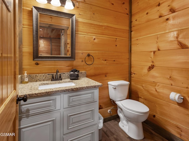 bathroom featuring hardwood / wood-style flooring, vanity, wood walls, and toilet