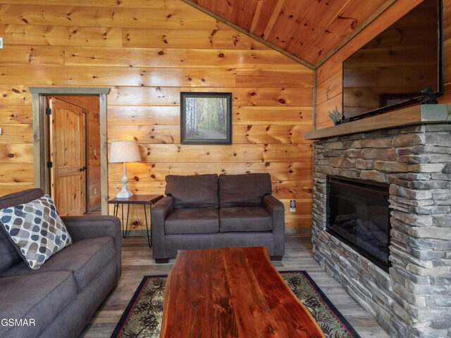 living room featuring wood ceiling, wooden walls, hardwood / wood-style floors, a stone fireplace, and lofted ceiling