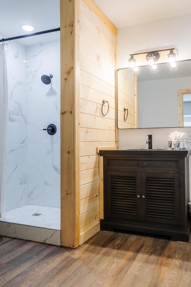 bathroom with walk in shower, wood walls, vanity, and wood finished floors