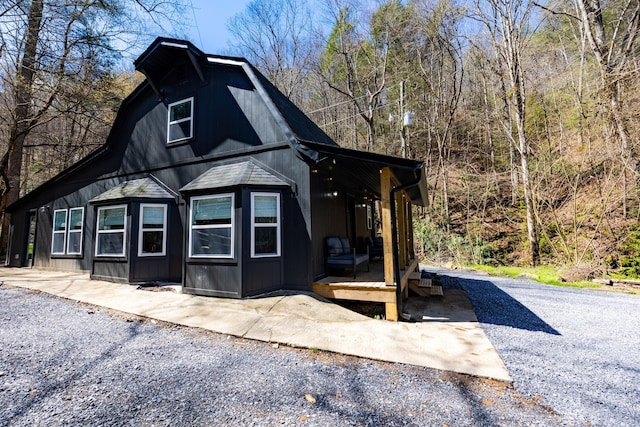 view of home's exterior with covered porch, roof with shingles, and a gambrel roof