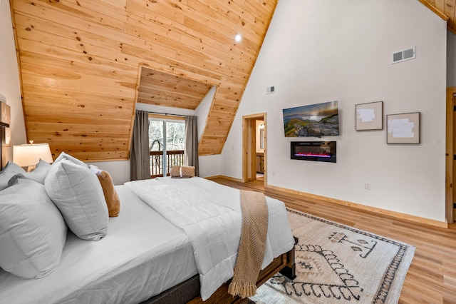 bedroom featuring access to exterior, visible vents, a glass covered fireplace, wood finished floors, and high vaulted ceiling