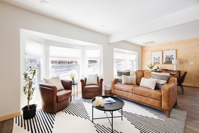 living room with wooden walls, baseboards, visible vents, wood finished floors, and beam ceiling