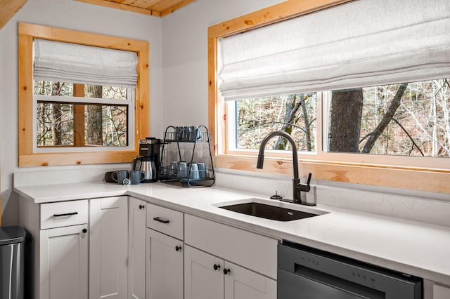 kitchen with light countertops, white cabinets, a sink, and dishwasher