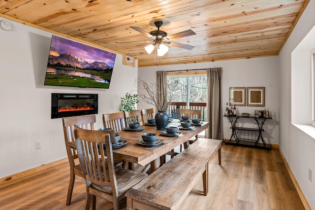 dining room with a glass covered fireplace, wood finished floors, wood ceiling, and baseboards