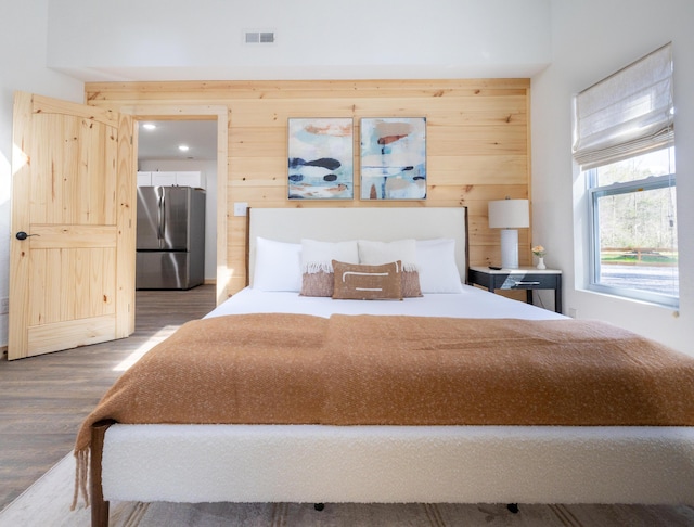 bedroom featuring visible vents, wood finished floors, freestanding refrigerator, and wooden walls