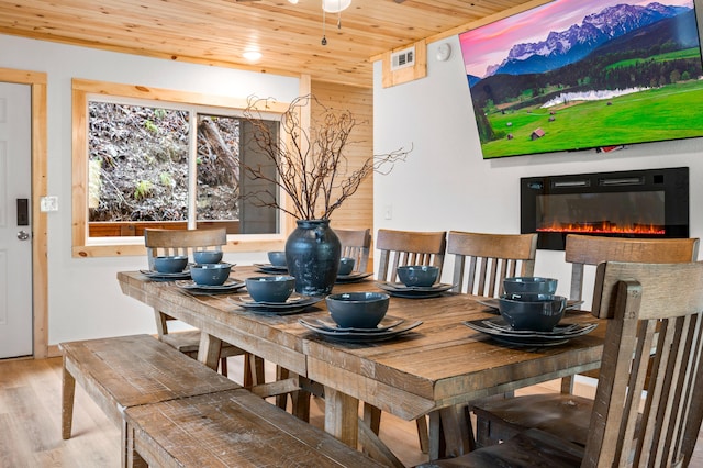 dining area featuring wood walls, wood finished floors, visible vents, wood ceiling, and a glass covered fireplace