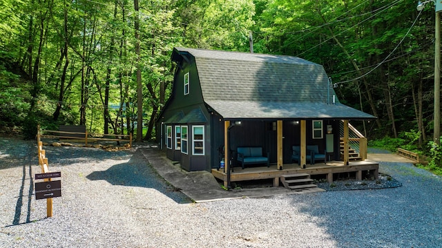 view of front of house with roof with shingles, a wooded view, and a gambrel roof