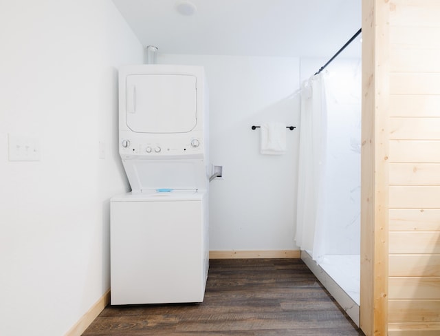 clothes washing area featuring dark wood-style floors, laundry area, stacked washer and clothes dryer, and baseboards