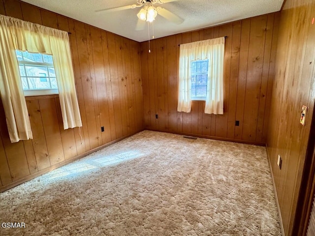 carpeted empty room with a textured ceiling, ceiling fan, and wood walls