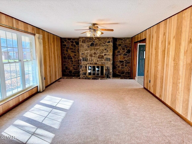 unfurnished living room featuring light colored carpet, a stone fireplace, ceiling fan, and wooden walls