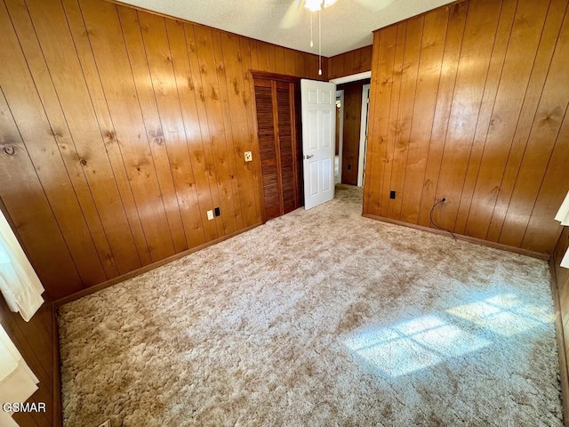 unfurnished bedroom featuring carpet flooring, ceiling fan, and wooden walls