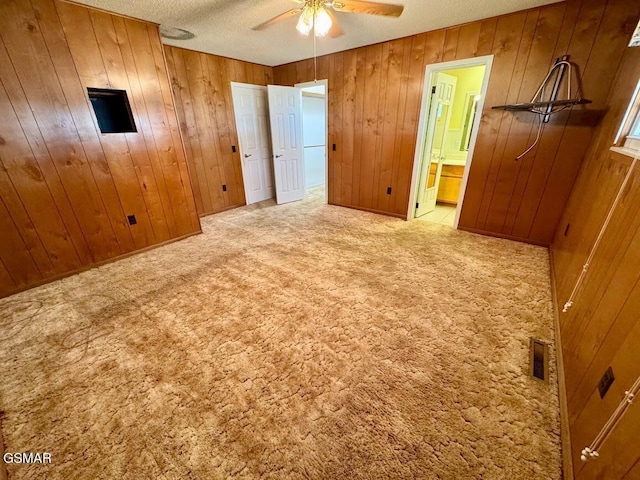 unfurnished bedroom with ceiling fan, ensuite bathroom, wood walls, a textured ceiling, and light carpet