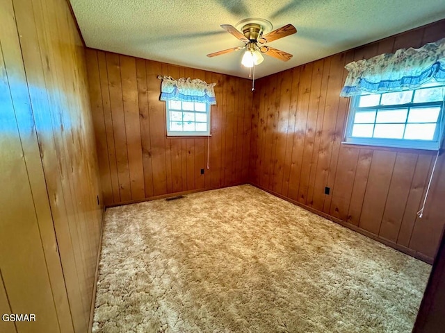 unfurnished room with carpet flooring, wooden walls, ceiling fan, and a textured ceiling