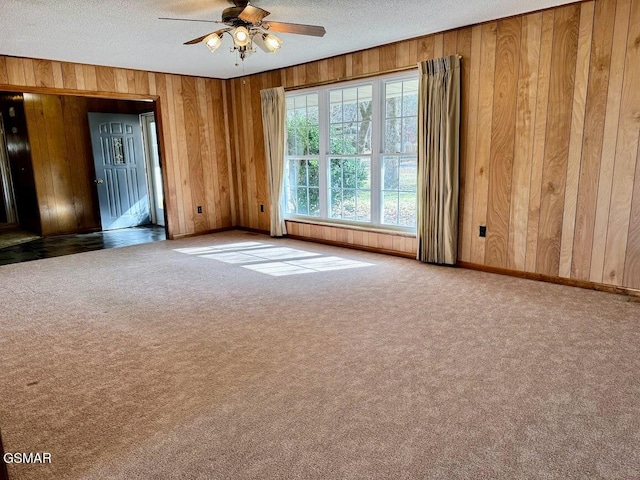 unfurnished room with a textured ceiling, ceiling fan, carpet floors, and wood walls