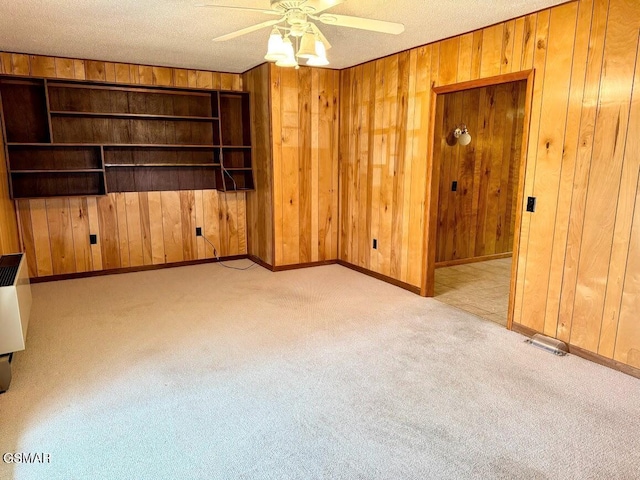 unfurnished living room featuring light carpet, wooden walls, ceiling fan, and a textured ceiling