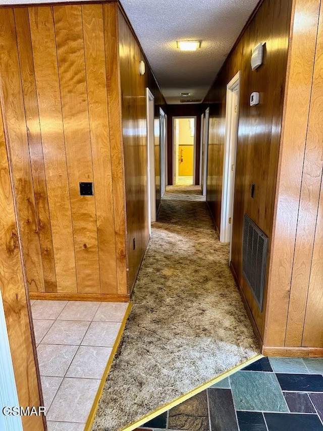 corridor featuring wooden walls, light colored carpet, and a textured ceiling