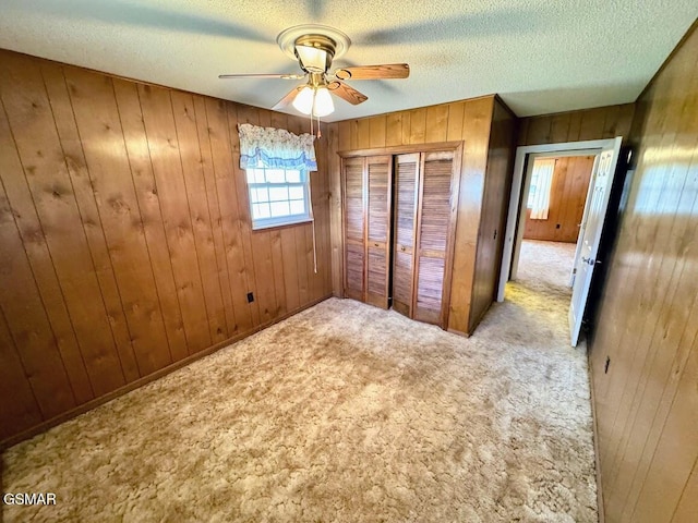 unfurnished bedroom featuring ceiling fan, light carpet, a textured ceiling, wooden walls, and a closet