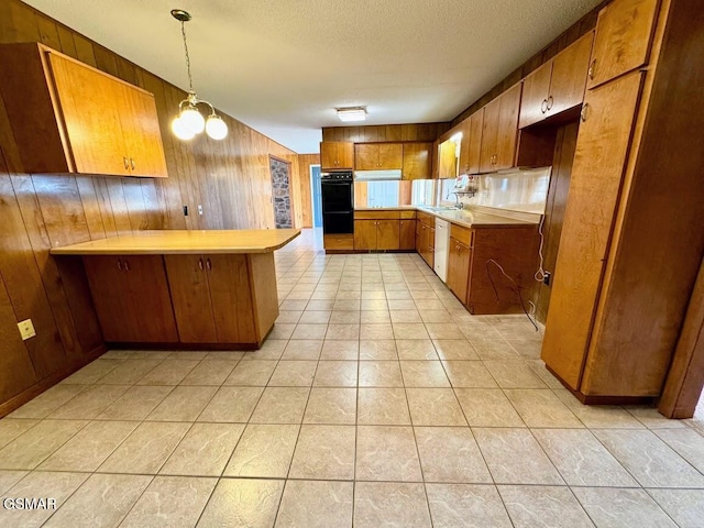 kitchen featuring pendant lighting, kitchen peninsula, black double oven, and wooden walls