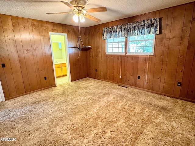 unfurnished room featuring ceiling fan, wood walls, carpet floors, and a textured ceiling