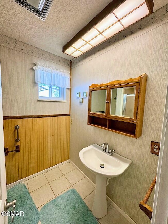 bathroom featuring tile patterned floors, wood walls, sink, and a textured ceiling