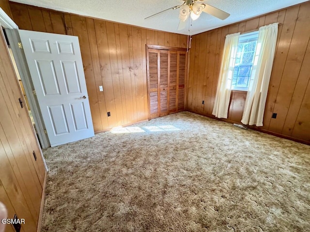 carpeted spare room featuring a textured ceiling, ceiling fan, and wooden walls