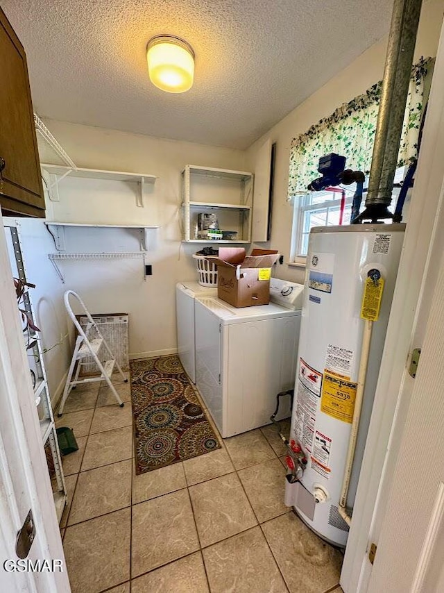 clothes washing area with cabinets, gas water heater, washing machine and dryer, a textured ceiling, and light tile patterned flooring