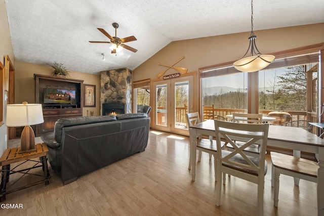 dining room featuring light wood-type flooring, a stone fireplace, a wealth of natural light, and lofted ceiling