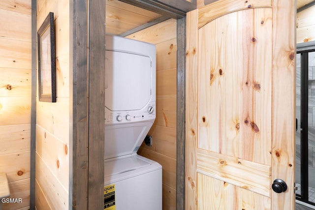 laundry area with laundry area, stacked washer / dryer, and wooden walls