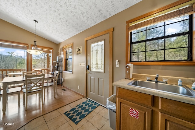 kitchen with lofted ceiling, light tile patterned floors, a textured ceiling, a sink, and decorative light fixtures