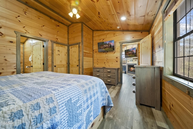 bedroom with lofted ceiling, a warm lit fireplace, wooden walls, wood ceiling, and hardwood / wood-style floors