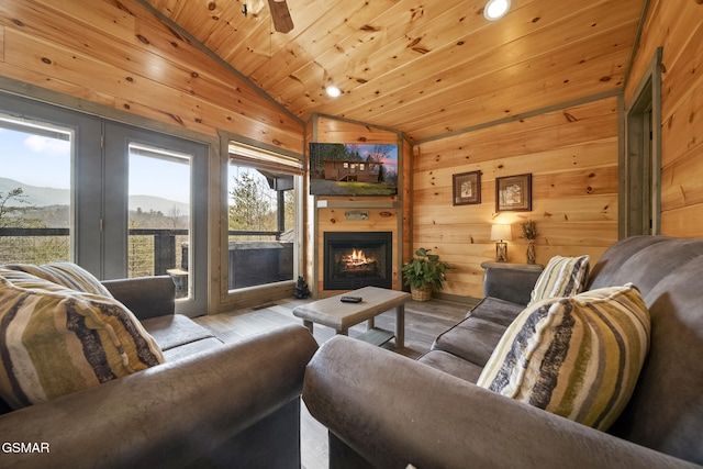 living area with lofted ceiling, wooden ceiling, a lit fireplace, and wooden walls