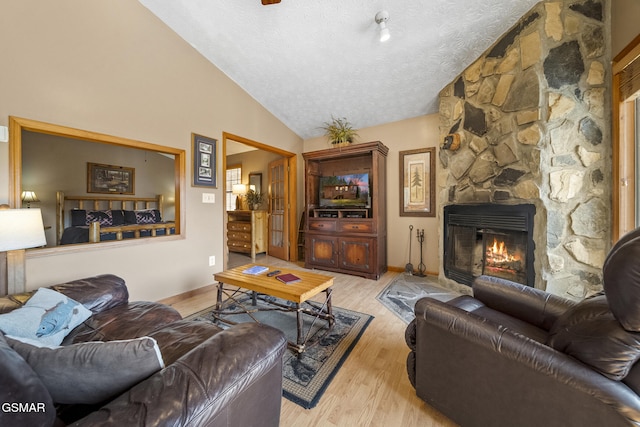 living area with light wood-style flooring, vaulted ceiling, a stone fireplace, a textured ceiling, and baseboards