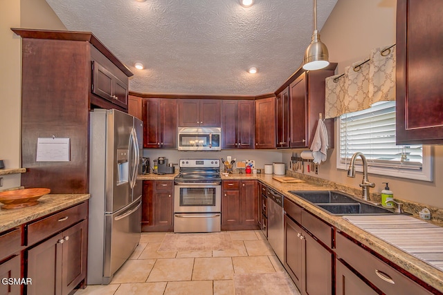 kitchen featuring appliances with stainless steel finishes, hanging light fixtures, a textured ceiling, light tile patterned floors, and sink