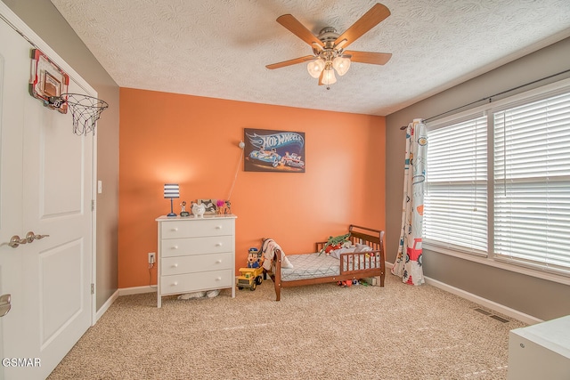 bedroom featuring ceiling fan, carpet flooring, a crib, and a textured ceiling