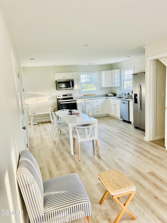 kitchen with appliances with stainless steel finishes, white cabinets, and light hardwood / wood-style floors