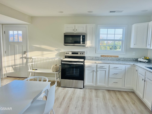 kitchen featuring white cabinets, appliances with stainless steel finishes, light stone counters, and light hardwood / wood-style flooring