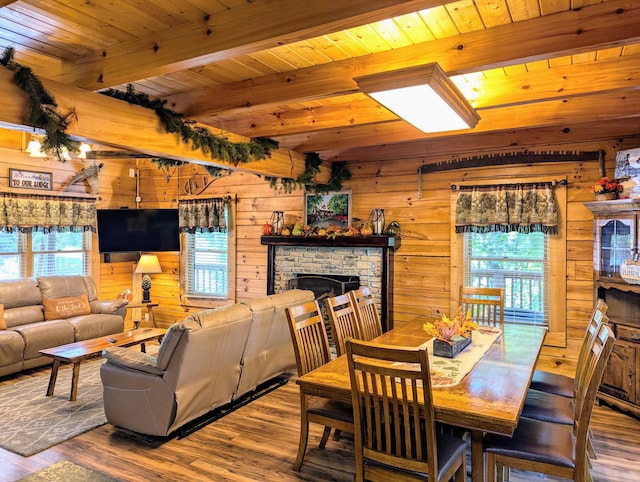 dining room with wood ceiling, wooden walls, beam ceiling, hardwood / wood-style floors, and a stone fireplace