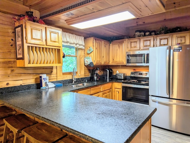 kitchen featuring stainless steel appliances, a peninsula, wood walls, a sink, and wood ceiling