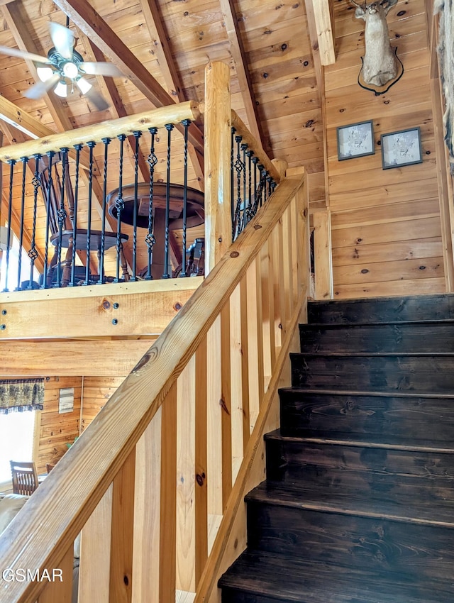 staircase with a ceiling fan, wooden ceiling, vaulted ceiling with beams, and wooden walls